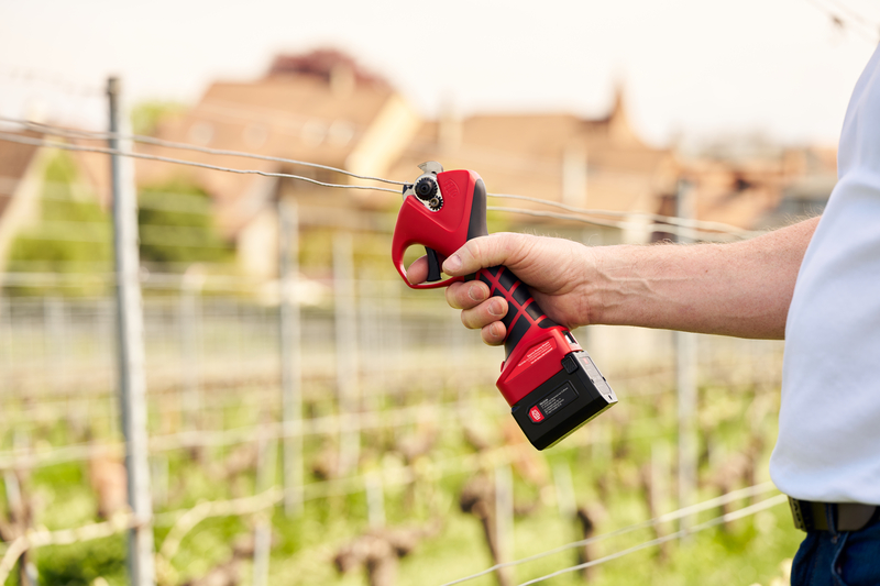 Hands using red-handled cable cutters on a copper cable