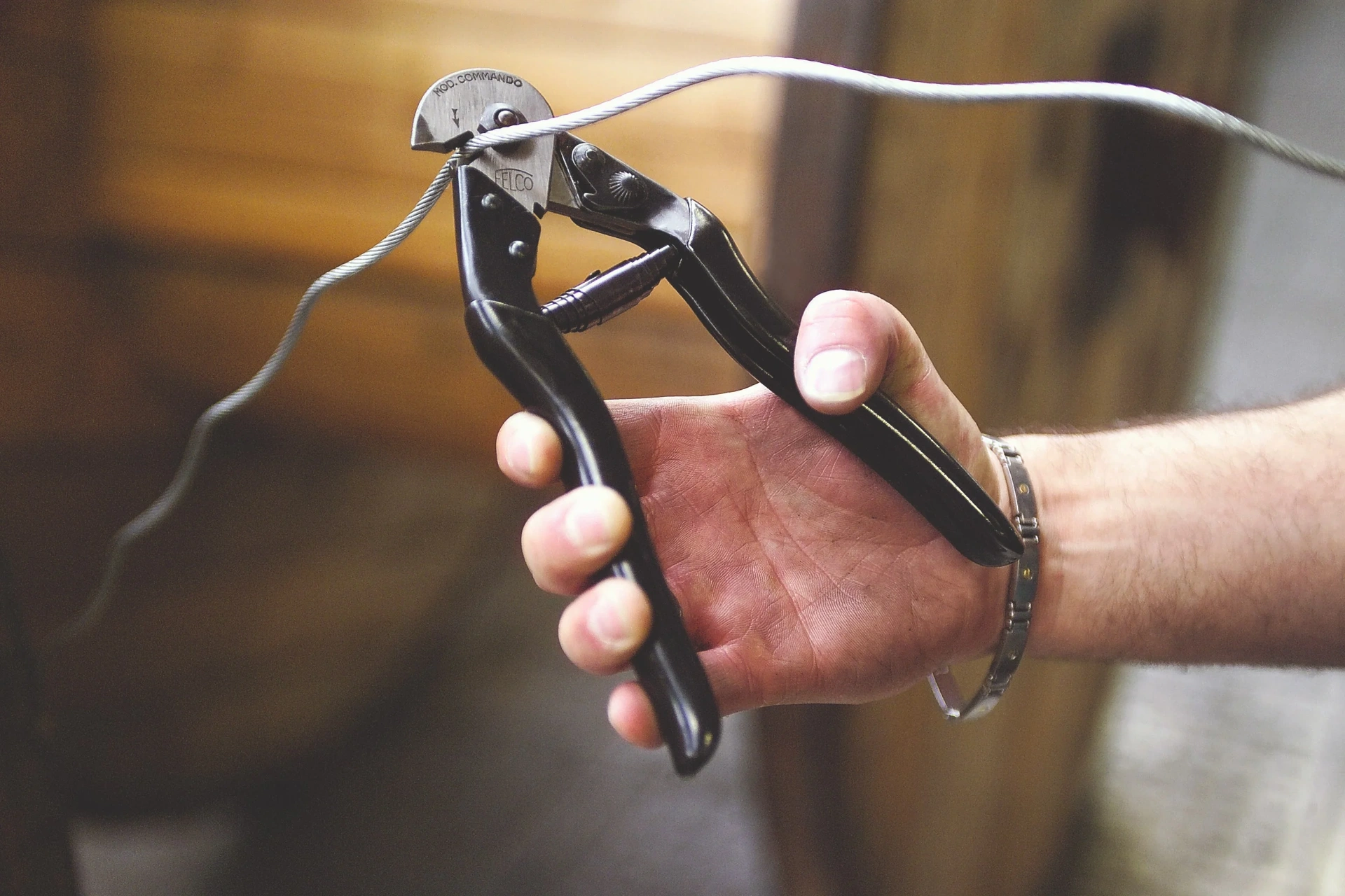 Hands using red-handled cable cutters on a copper cable